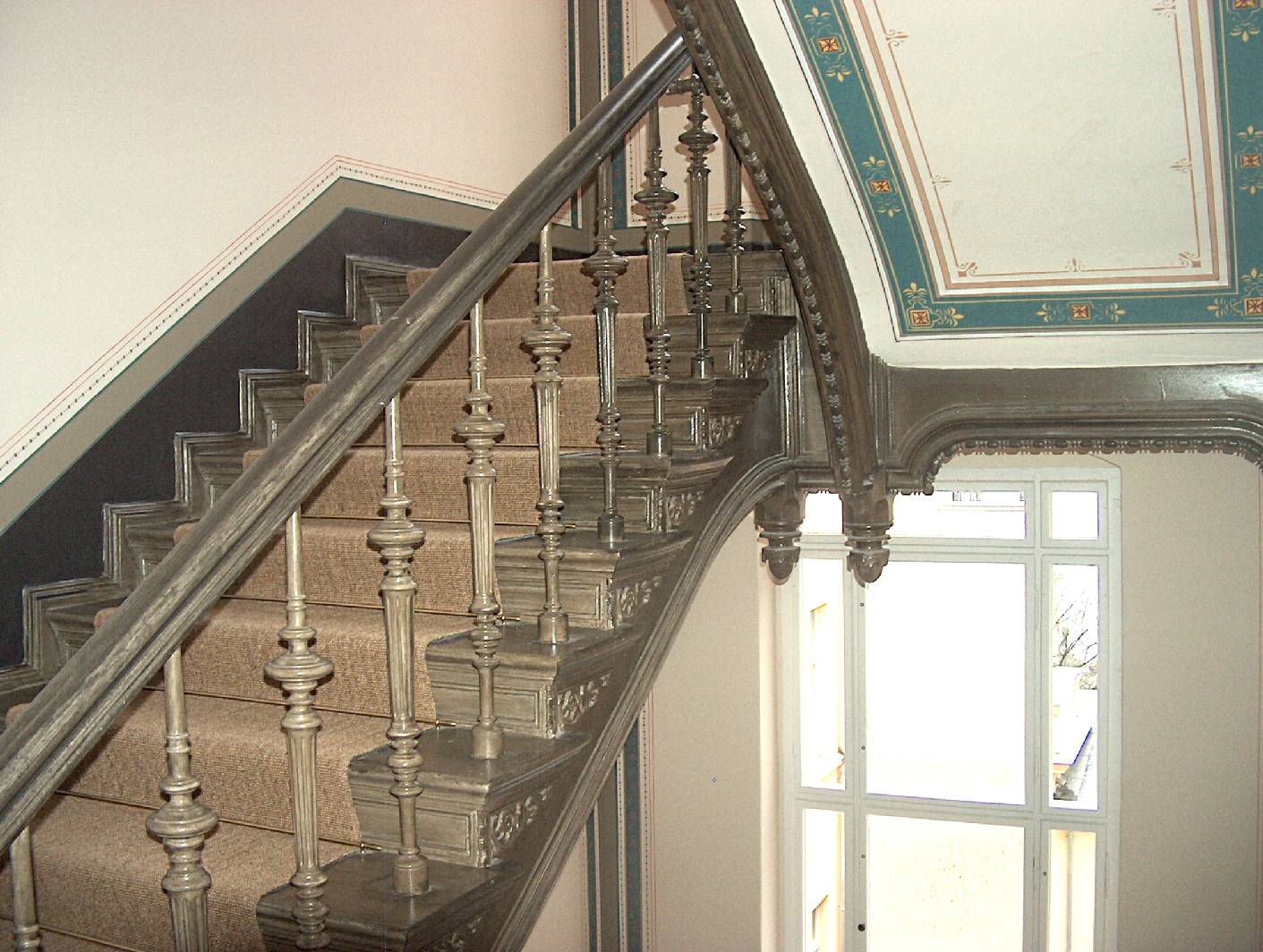 Nach dem Freilegen der Holzbauteile im Treppenhaus konnte ermittelt werden welchen Duktus die Holzimitation hatte. Der als Restaurator für historische Malerei arbeitende Malermeister Schimpf hat die Holzmalerei aus der ersten Fassung der Freilegung übernommen. Bevor die  Holzmalerei aufgebracht wurde hat Norbert Schimpf die dafür Notwendigen Malerarbeiten übernommen. Zu sehen ist auch die Deckenmalerei im Treppenhaus. Die Firma Restaurierung und Gestaltung / exklusive Malerarbeiten hat alle Deckenmalereien an den Lauf und Podestdecken rekonstruiert.