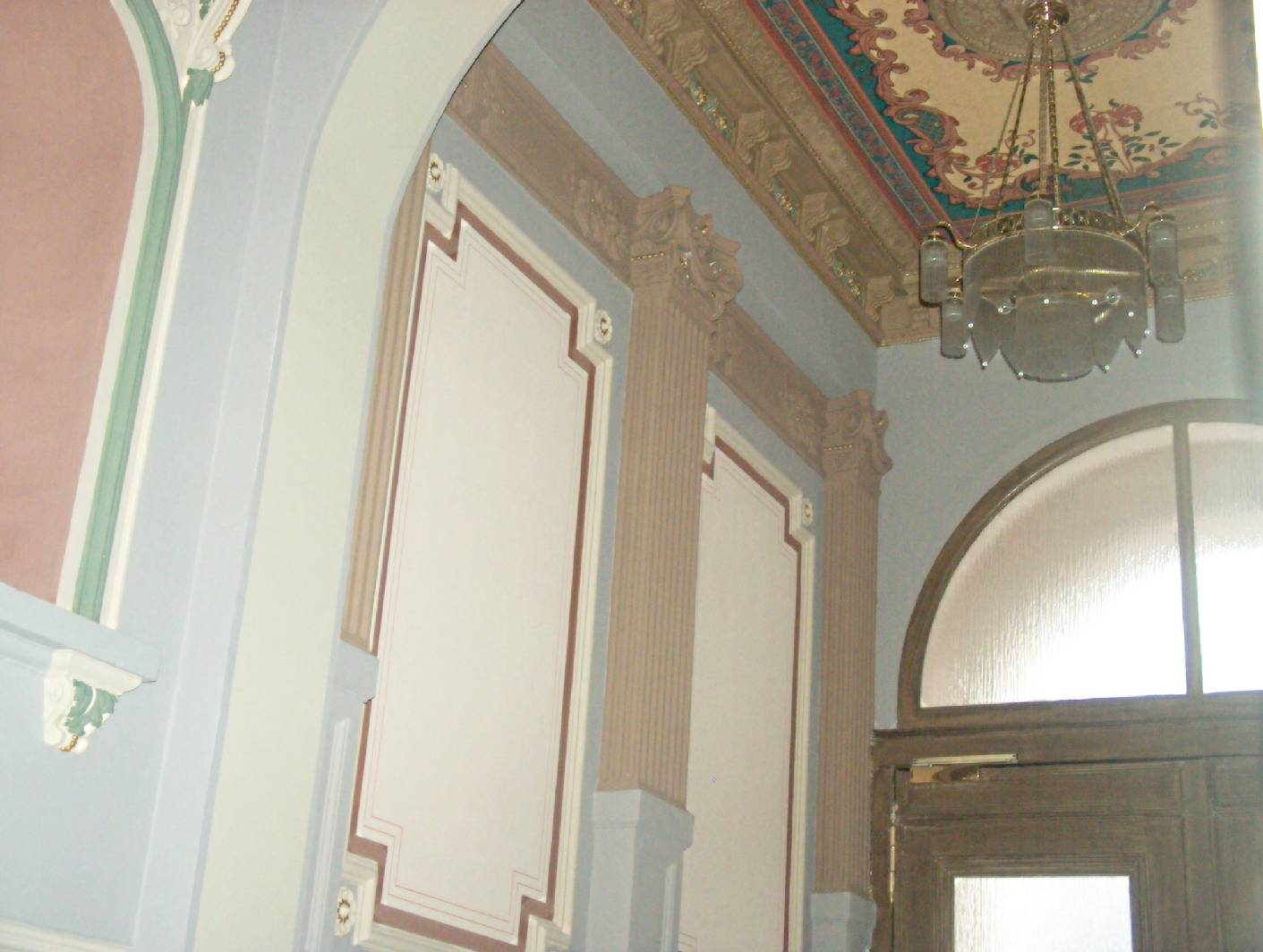 Zu sehen ist das Ensemble einer Deckenmalerei und einer Wandmalerei mit Eingangstor in Holzmalerei. Der Maler – Innungsbetrieb Gestaltet und Restauriert Treppenhäuser aus der Gründerzeit und stellt diese wieder so her, wie sie aussahen. Norbert Schimpf ist Malermeister und staatl. geprüfter Techniker für Farb- und Lacktechniken und hat sich auf die Arbeiten des Restaurator im Malerhandwerk Spezialist. Der Betrieb Restaurierung und Gestaltung exklusive Malerarbeiten stellt so gesamte Konzepte von den Vor- und Malerarbeiten bis zur Restaurierung im Treppenhaus und Altbau her. Der Malerbetrieb gehört zu den Betreiben der Berliner Malerinnung.